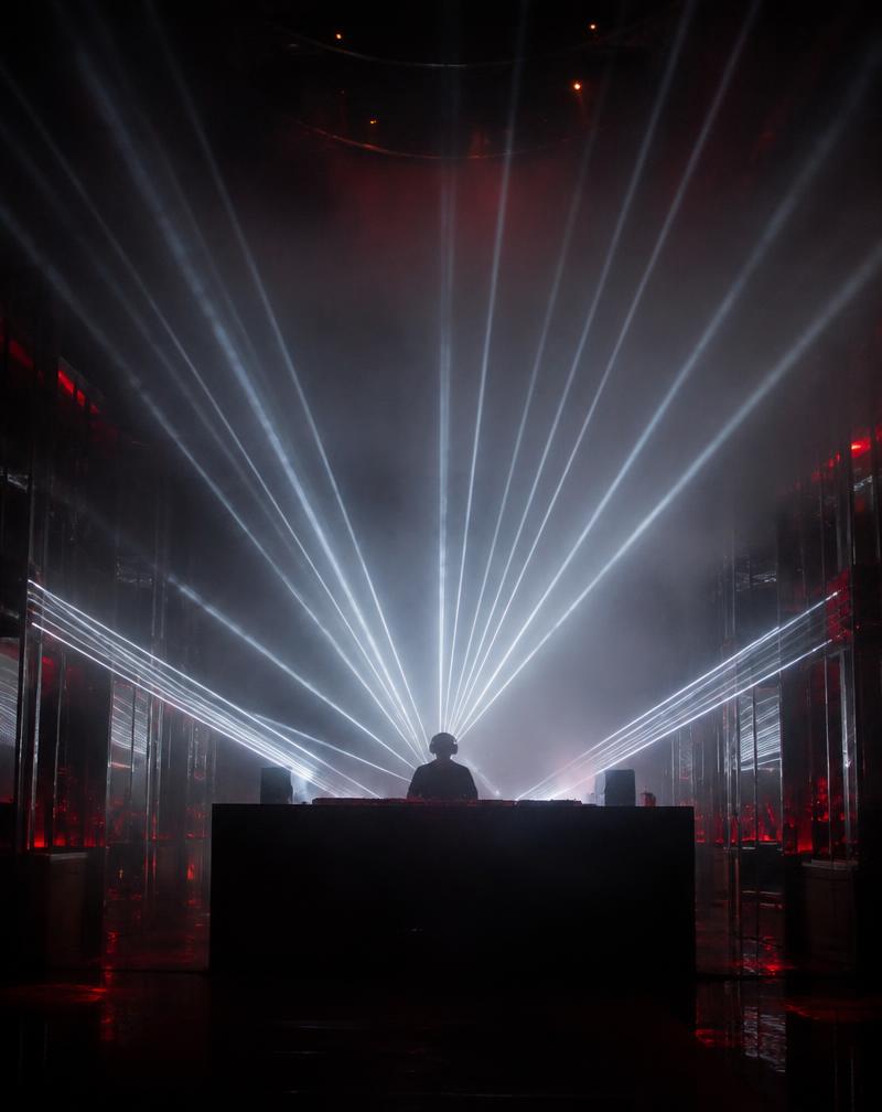 DJ silhouetted by a fan of white lasers